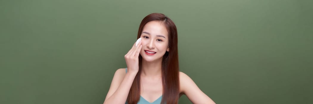 Girl applying lotion using cotton pad over green background, panorama, crop