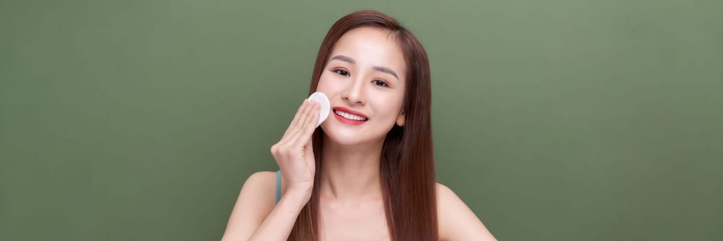 Girl applying lotion using cotton pad over green background, panorama, crop