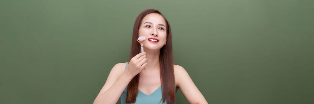 Woman using natural jade face roller on green background, web banner.