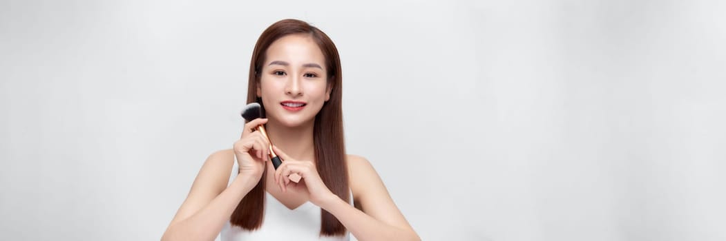 beautiful happy young girl with perfect skin is holding makeup brush in hand over banner background