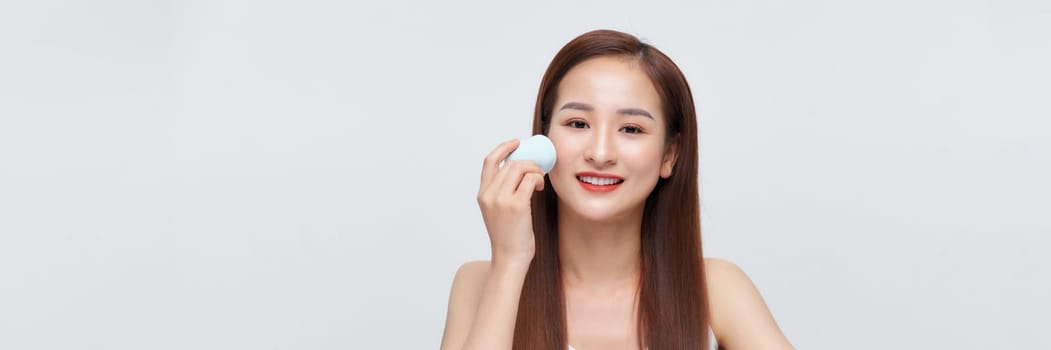 Beautiful young woman applying makeup using beauty blender sponge.