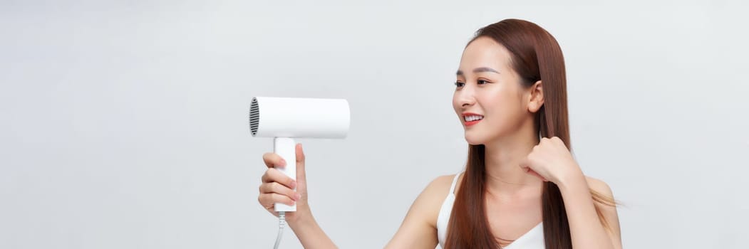 A cute young girl dries her beautiful long silky hair with a hair dryer. Banner