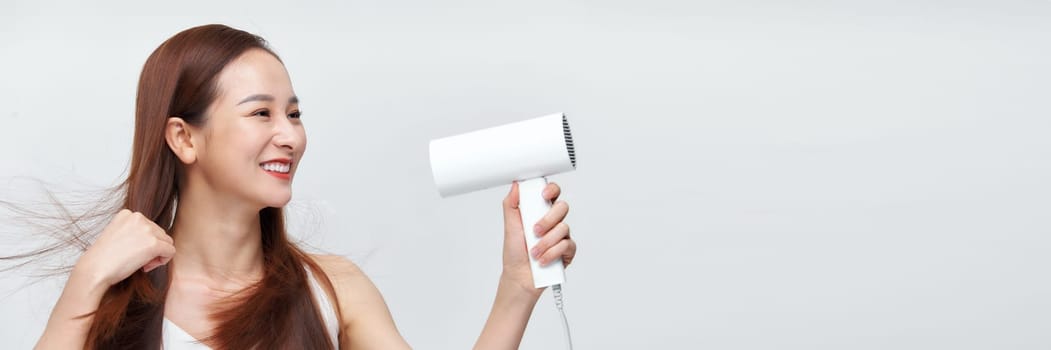 Woman dries her beautiful long hair with a hair dryer against a white background. Web banner