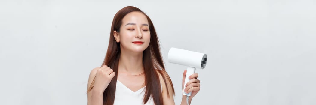 Banner of young asian woman using hair dryer on white background
