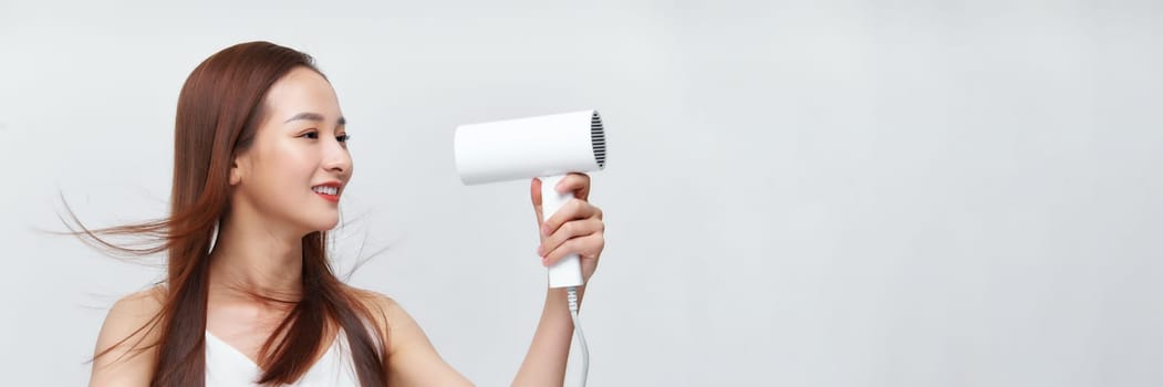 A cute young girl dries her beautiful long silky hair with a hair dryer. Banner