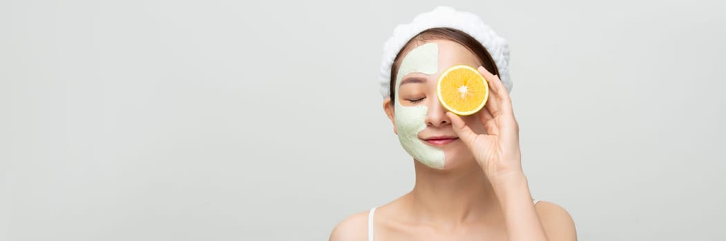 Banner with beautiful happy girl applying mud mask showing a juicy orange on white