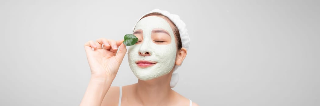 Young girl enjoys clay facial mask posing with a leaf on white banner.