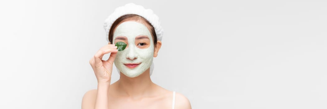 Young girl with a cleansing cosmetic mask on her face poses with a green leaf. Banner
