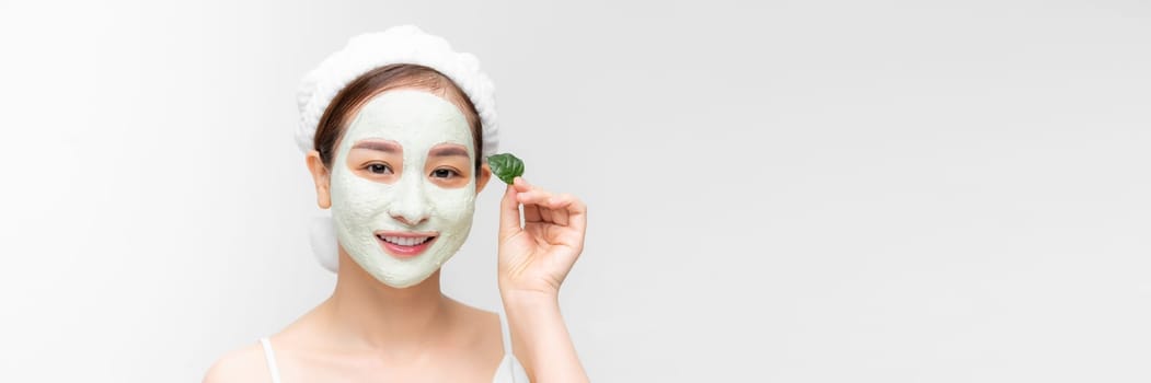 A woman with white nourishing mask on face and green leaf in hand, white banner isolated.