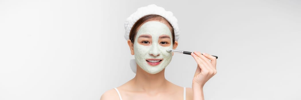  Happy young woman applying a white mask on her face with a brush.