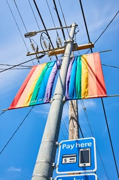 Image of Upward view of two rainbow banners on street light pole with bright blue sky above