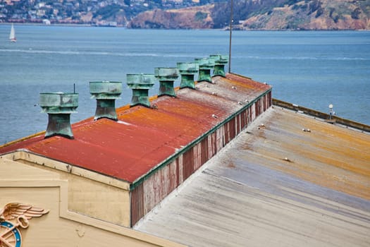 Image of Rooftop of warehouse in San Francisco Bay with seagulls resting on top and sailboat on water