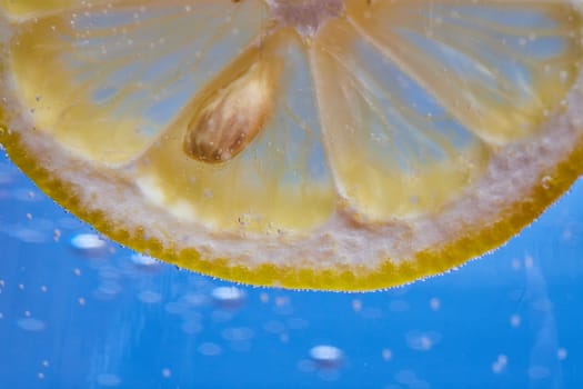 Image of Macro shot of curved edge of see through lemon slice with seed on blue background