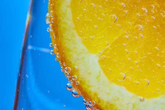 Image of Macro of orange slice covered in bubbles inside clear glass with blue background