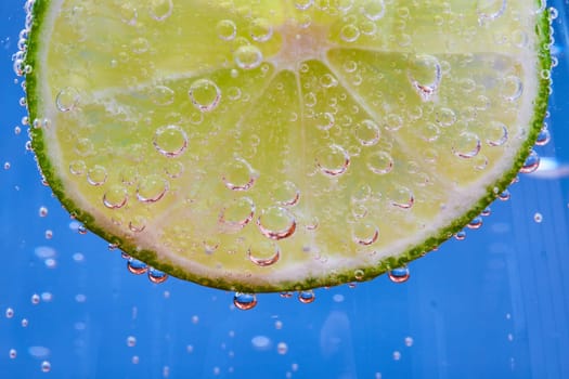 Image of Macro of fizzy bubbles on green lime slice against blue background