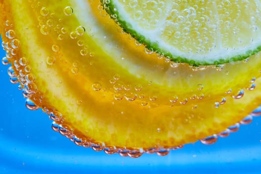 Image of Macro of citrus fruit slices covered in tiny silvery bubbles in clear glass with blue background