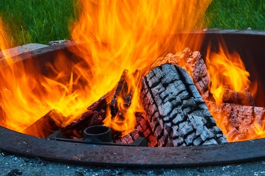 Image of Round fire pit with intense yellow and orange flames and black log with white ashen sides