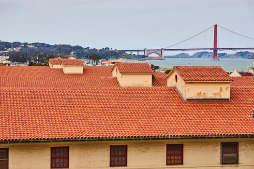 Image of Yellow building with red trim around windows and orange clay shingle roofs with Golden Gate Bridge