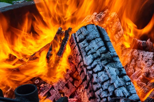 Image of Intense flames surrounding logs inside round fire pit with exposed white ashen log close up