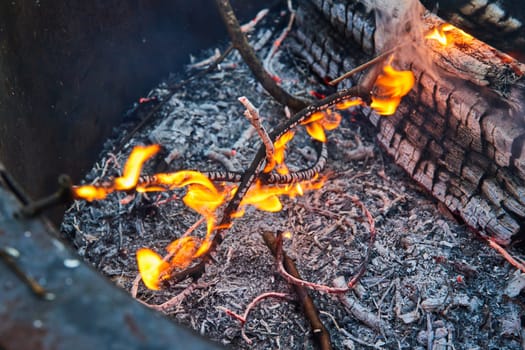Image of Close up of small twigs on fire with orange and yellow flames and red ashen embers below