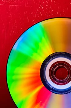 Image of Colorful CD on red background with bursts of rainbow colored lights across silvery surface