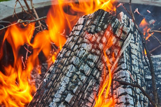 Image of Close up of burning ashen log with orange and yellow flames in round fire pit