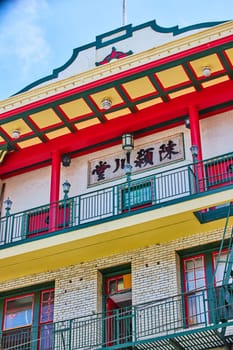 Image of Red beams and yellow and green trim on Chinese building with green fire escape and blue sky