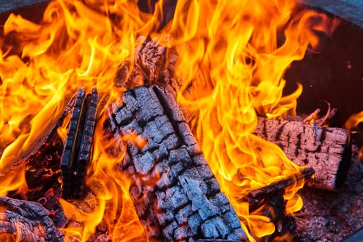 Image of Close up of charred and burning logs inside intense fire with orange and yellow flames in fire pit