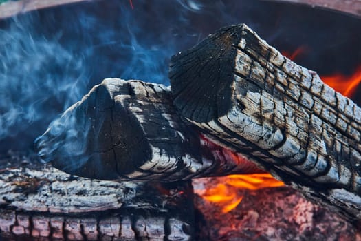 Image of Smoking ends of burnt logs with orange and yellow flames below close up background asset