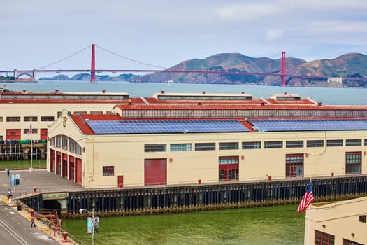 Image of Warehouses on pier with American flag and Golden Gate Bridge in distance
