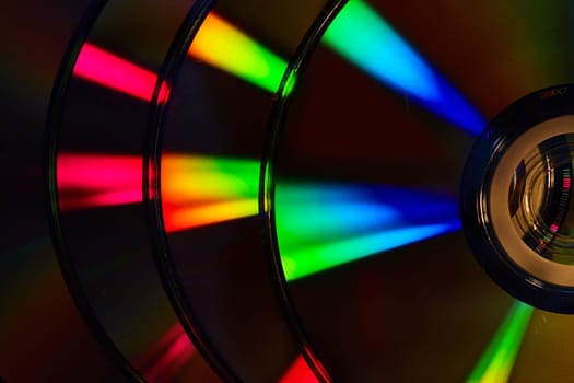 Image of Abstract stack of four dark silvery CDs with reflective rainbow colored bursts of light on surface