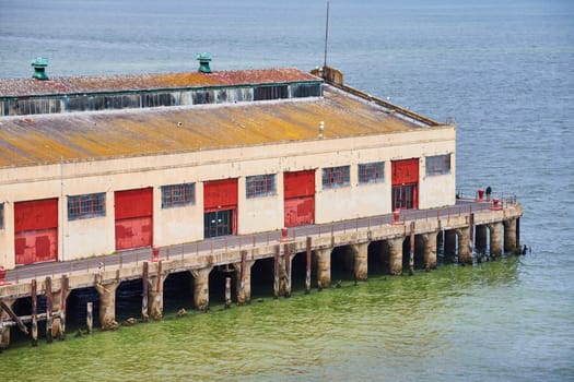 Image of Pier with warehouse and red bay doors with person against railing and seagull on roof