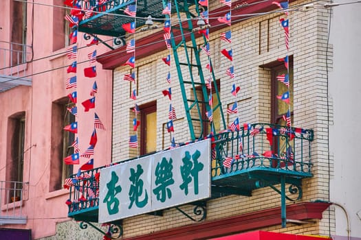 Image of White and green sign attached to green fire escape with American and Chinese flags