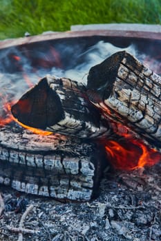 Image of Ashen logs in dying fire inside round fire pit with smoke billowing background asset