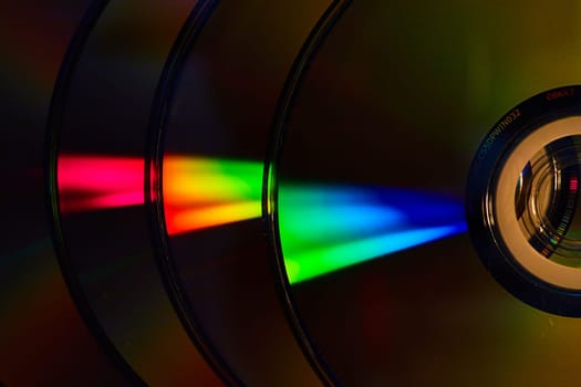 Image of Abstract stack of four dark silvery CDs with reflective rainbow bursts of light on surface