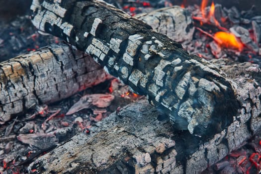 Image of Black charred log with cracked ashen surface and red embers below with tiny orange flames