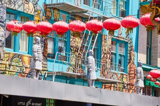 Image of Red paper lanterns hanging in front of Chinese wall mural with soldier statues