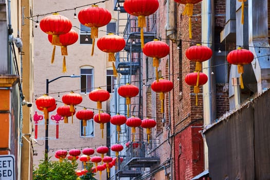 Image of Strings of Chinese paper lanterns hanging from wires attached to buildings and fire escapes