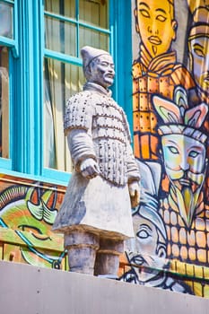 Image of Chinese statue of man standing in front of soldier mural with bright blue windows