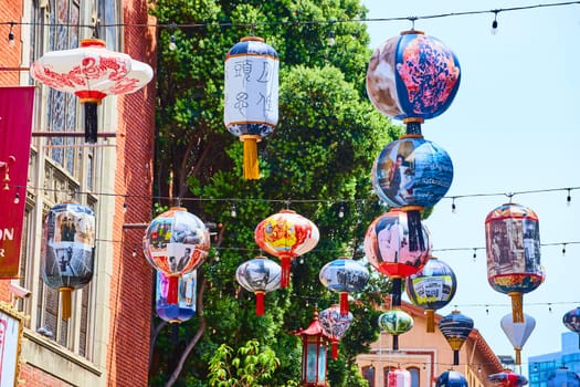 Image of Colorful Chinese paper lanterns on long chains with lights and tree in background