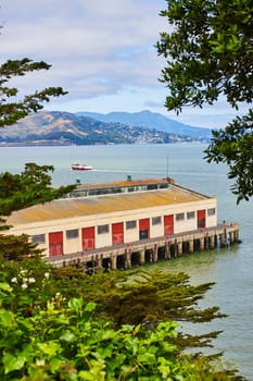 Image of Trees framing a warehouse on a dock with a tour boat on San Francisco Bay