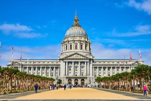 Image of Purple clouds behind San Francisco city hall on blue sky day with sandy crowded entrance