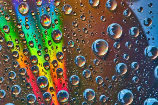 Image of Brilliant slash of rainbow light across silver metal surface with rainbow flames inside waterdrops