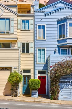 Image of Two houses touching side by side one blue and one yellow with shrub in middle spot