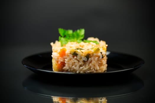 Cooked boiled rice with zucchini, carrots and vegetables in a plate, isolated on a black background.