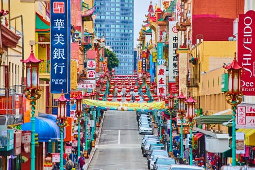 Image of Vibrant Chinatown view of crowded sidewalks and row of parked cars with hanging lanterns and signs