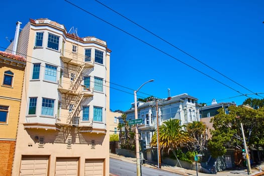 Image of Pale yellow house with bay windows and fire escape off 15th street on blue sky day