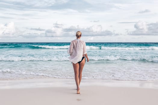 Woman wearing white loose tunic over bikini on Mahe Island, Seychelles. Summer vacations on picture perfect tropical beach concept.