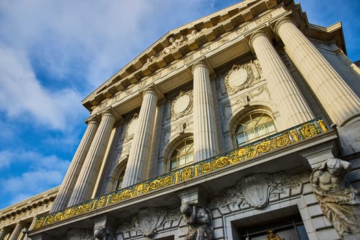 Image of Golden trim on government building on cloudy blue sky day with sun hitting city hall