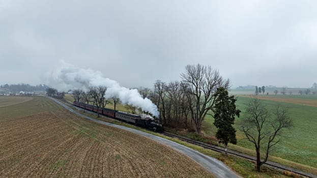 A vintage steam engine chugs along the track, surrounded by bare trees and fields on a misty morning in Pennsylvania. The scene captures the essence of a nostalgic train journey.